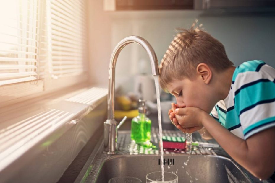 A young boy drinking water from the tap.