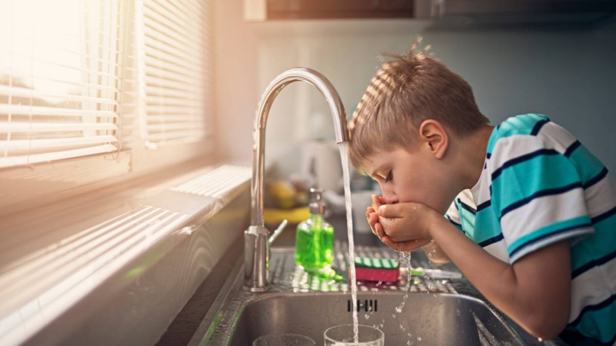 A young boy drinking water from the tap.
