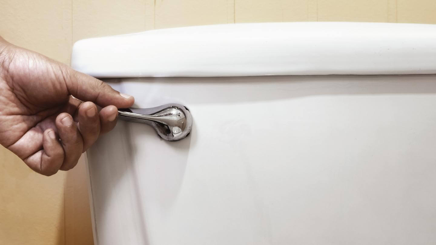 A hand on the handle of the toilet, trying to flush it.